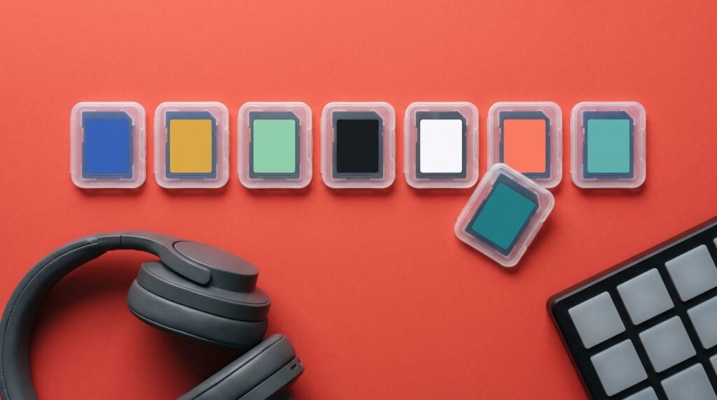 A row of colorful memory cards on a red surface with one card pulled out of the row, next to headphones and a pad controller