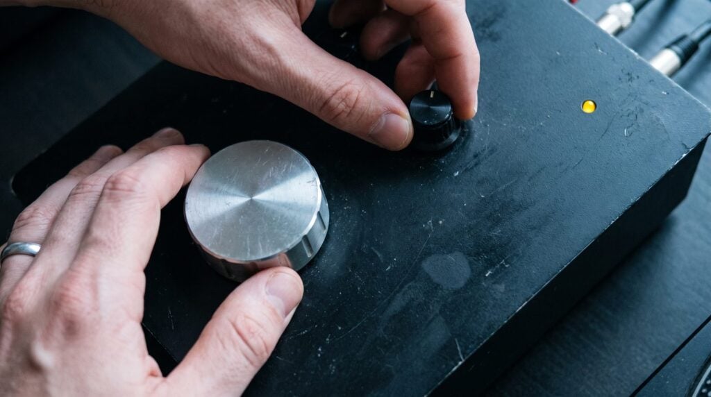 A DJ's hands turning the volume knobs of a plain black rotary mixer during an afternoon soundcheck