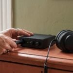 A man's hands plugging a microphone cable into a small audio interface next to closed-back headphones on a terracotta dresser