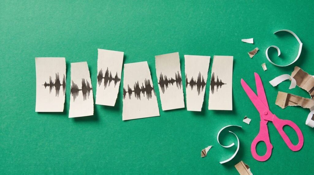 Paper collage of a printed waveform cut into seven slices and glued back in a new order on green paper, with pink paper scissors beside it